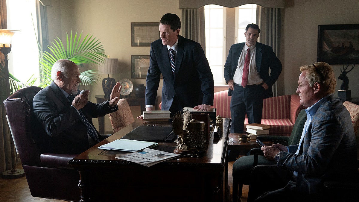 Gerald McRaney, Noah Emmerich, Paul Schneider, and Jason Clarke sit and stand around a large wooden desk during a tense office scene in Murdaugh: Death in the Family.