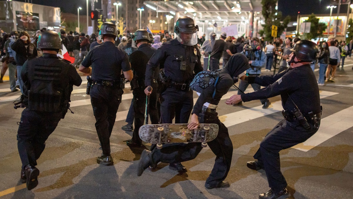 A person with a skateboard is detained by police during a protest in downtown Los Angeles