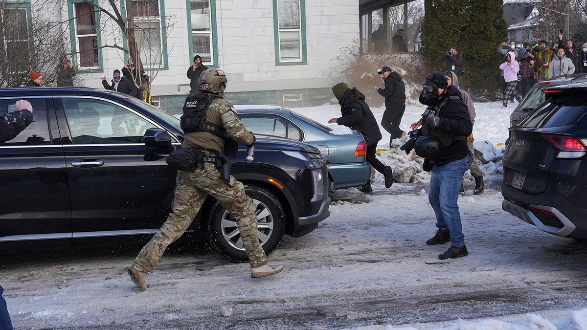 An officer runs towards protesters blocking vehicles and throwing snowballs
