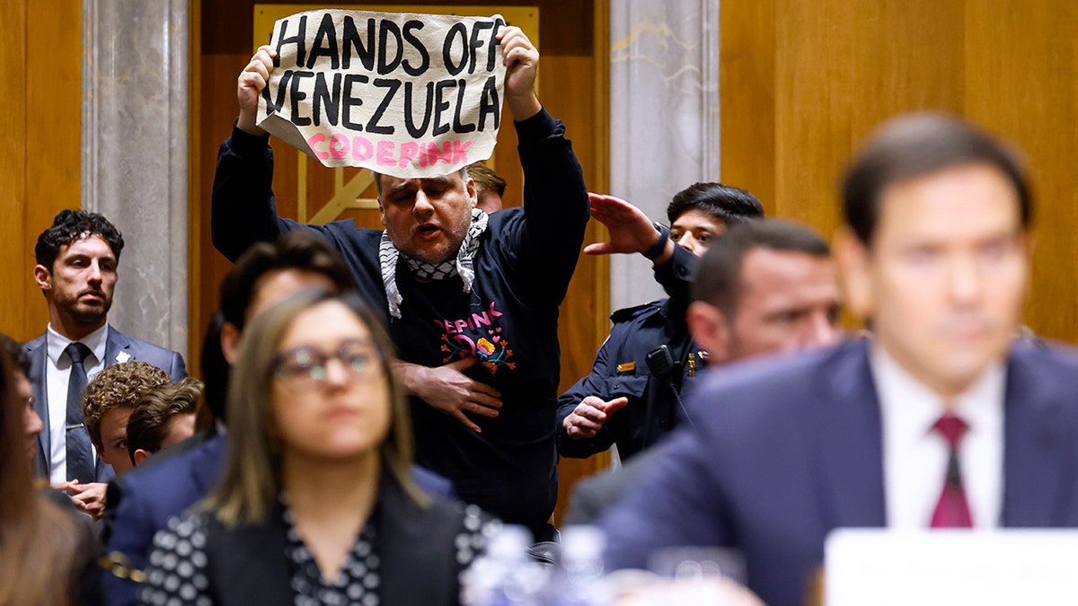 Demonstrator holds up sign as Secretary of State Marco Rubio testifies about Venezuela operations