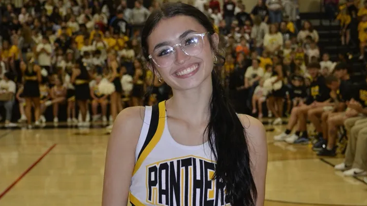 Kimber Mills, an Alabama high school cheerleader, smiles while wearing her cheer uniform at a school event