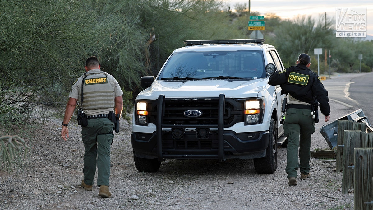 Sheriffs walk from a culvert near Nancy Guthrie's home is filled with various discarded items and debris in an outdoor area.