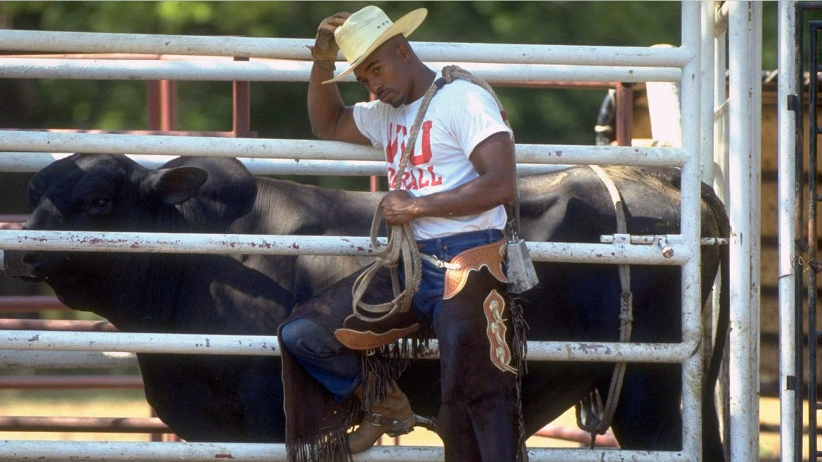 A young Leshon Johnson poses next to a bull in rodeo gear