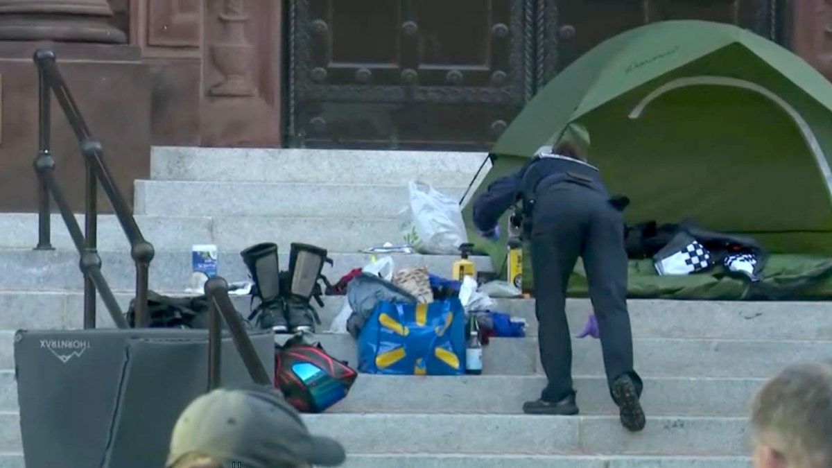 investigator looking through suspect's belongs near green tent on steps of Cathedral