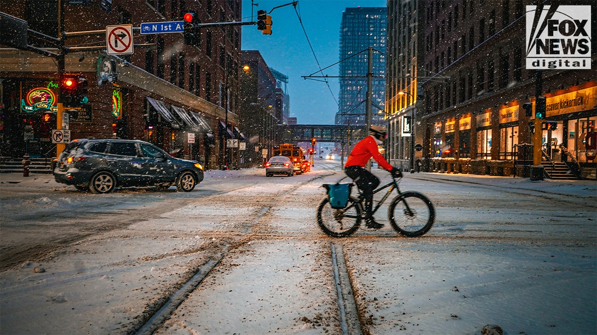 Bicyclist crossing a snowy downtown Minneapolis street at night.