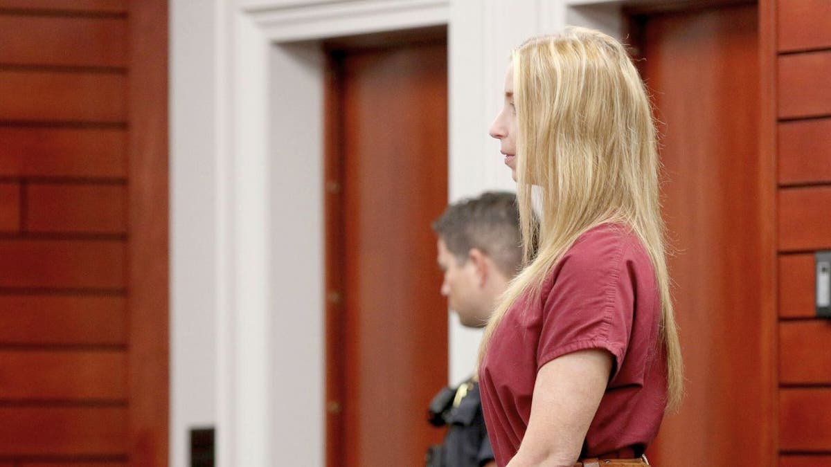 Julie Rizzitello stands in court wearing a red jail uniform and restraint belt.