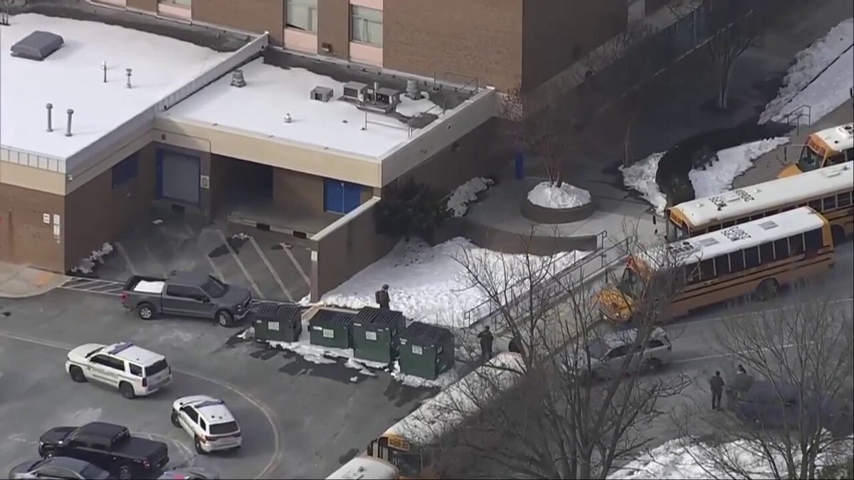 Police officers stand near vehicles and school buses in a school parking lot after a shooting.