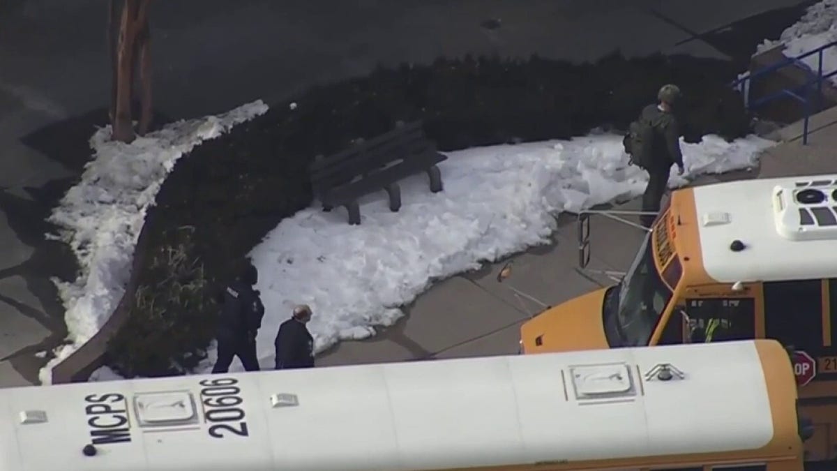 Officers walk near school buses outside a high school during an active police response.